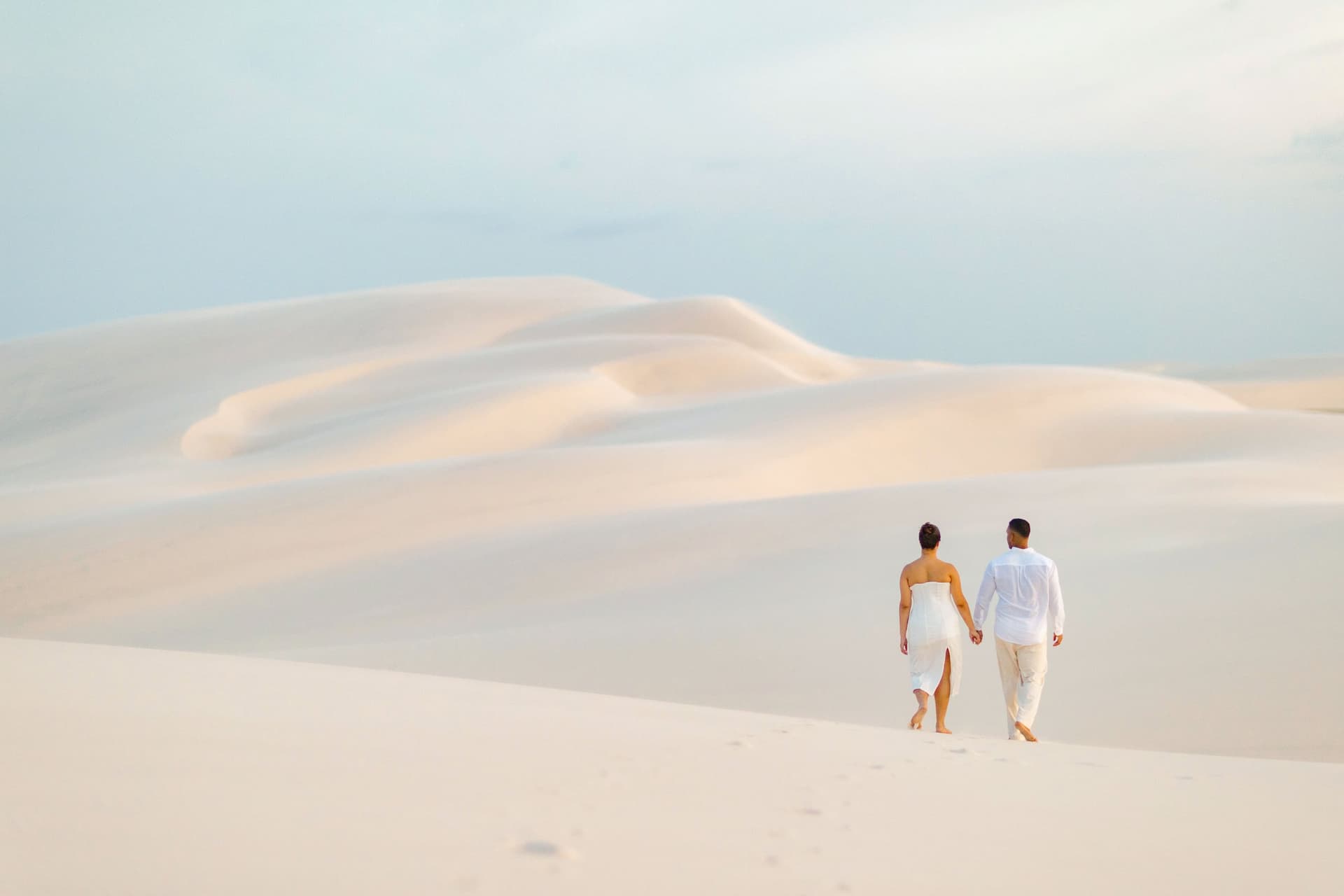 Casal caminhando descalço pelas dunas brancas dos Lençóis Maranhenses