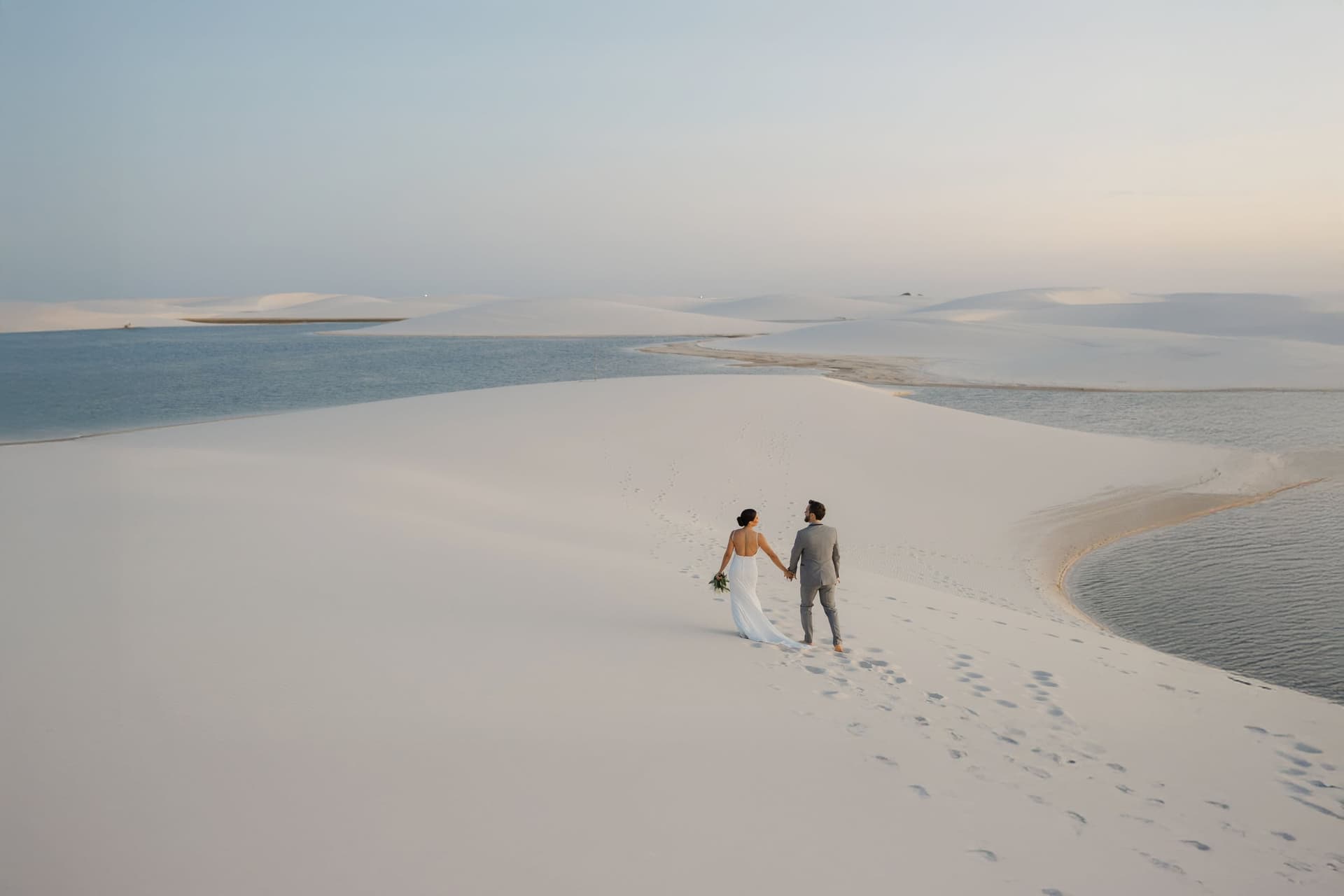 Casal caminhando entre dunas e lagoas dos Lençóis Maranhenses