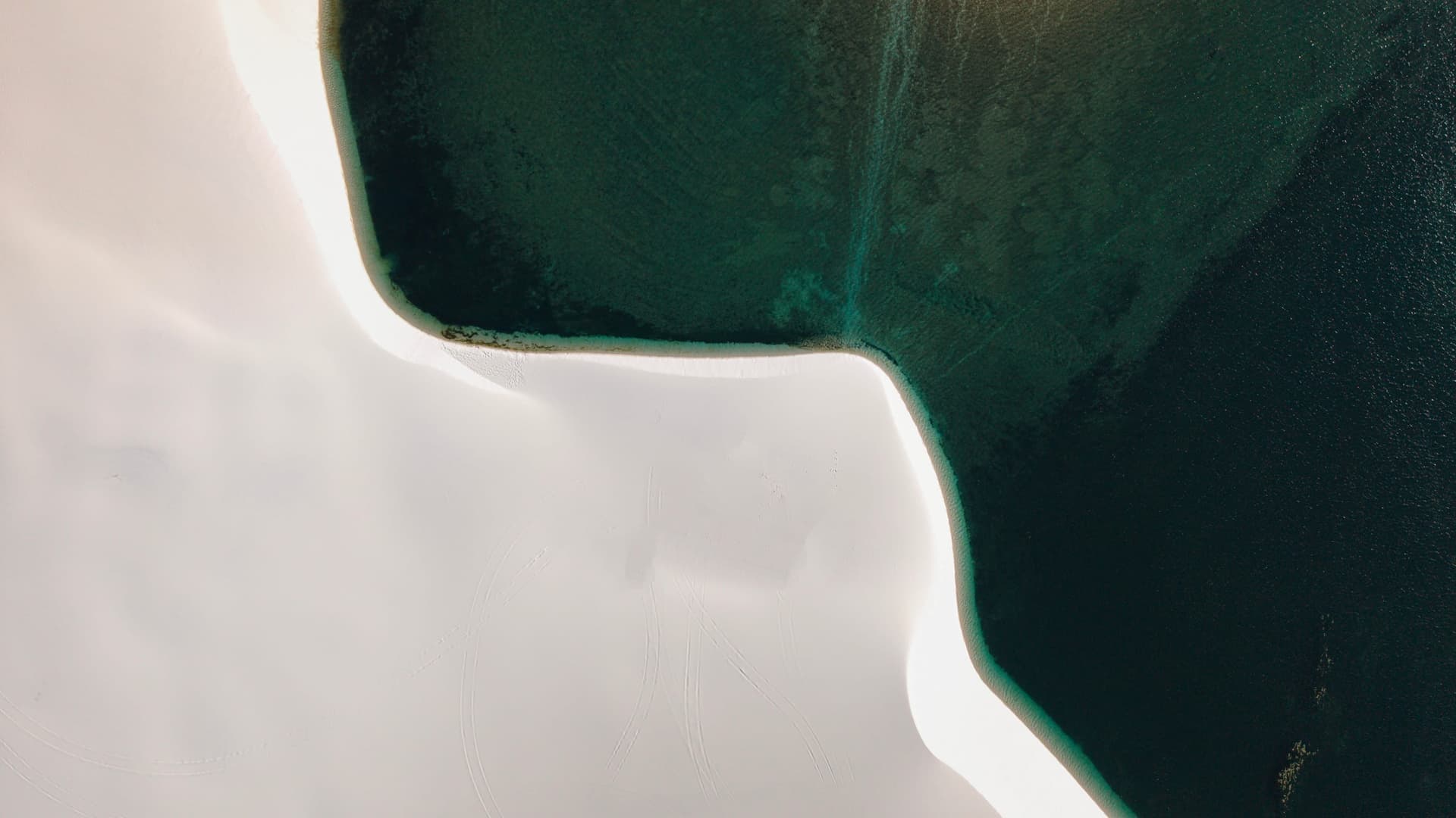 Duna branca desenhando uma curva na lagoa verde em Santo Amaro do Maranhão, vista aérea